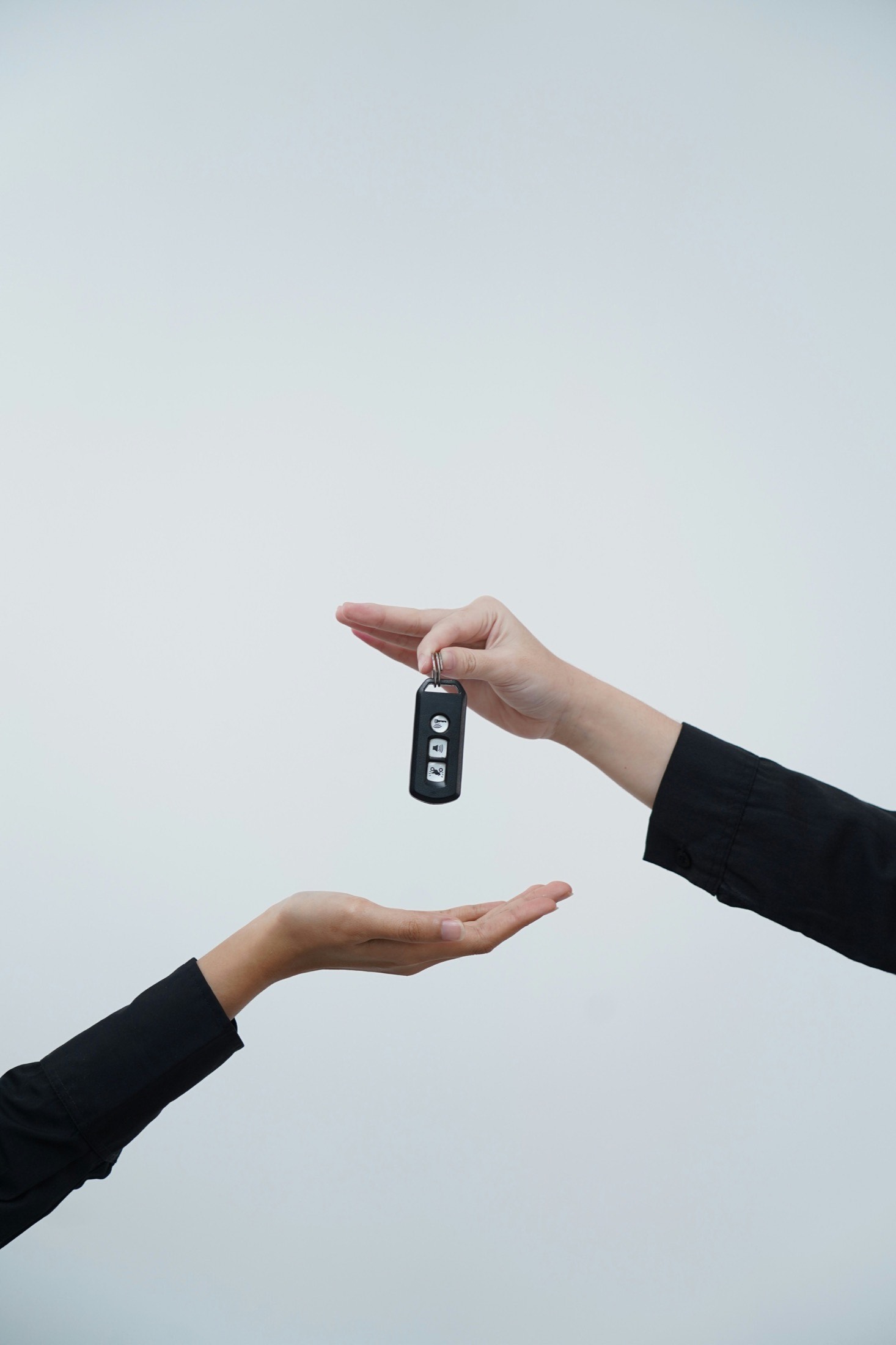 Hands exchanging a car key, representing a completed vehicle purchase.