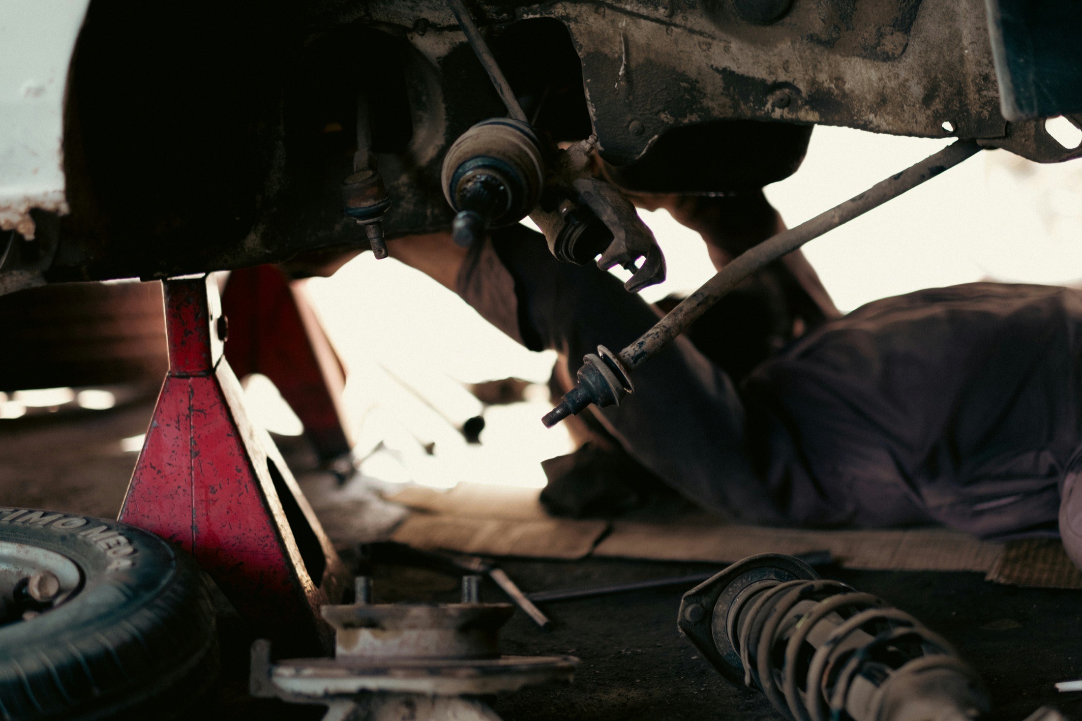 A certified technician working underneath a vehicle on a lift in the service bay.